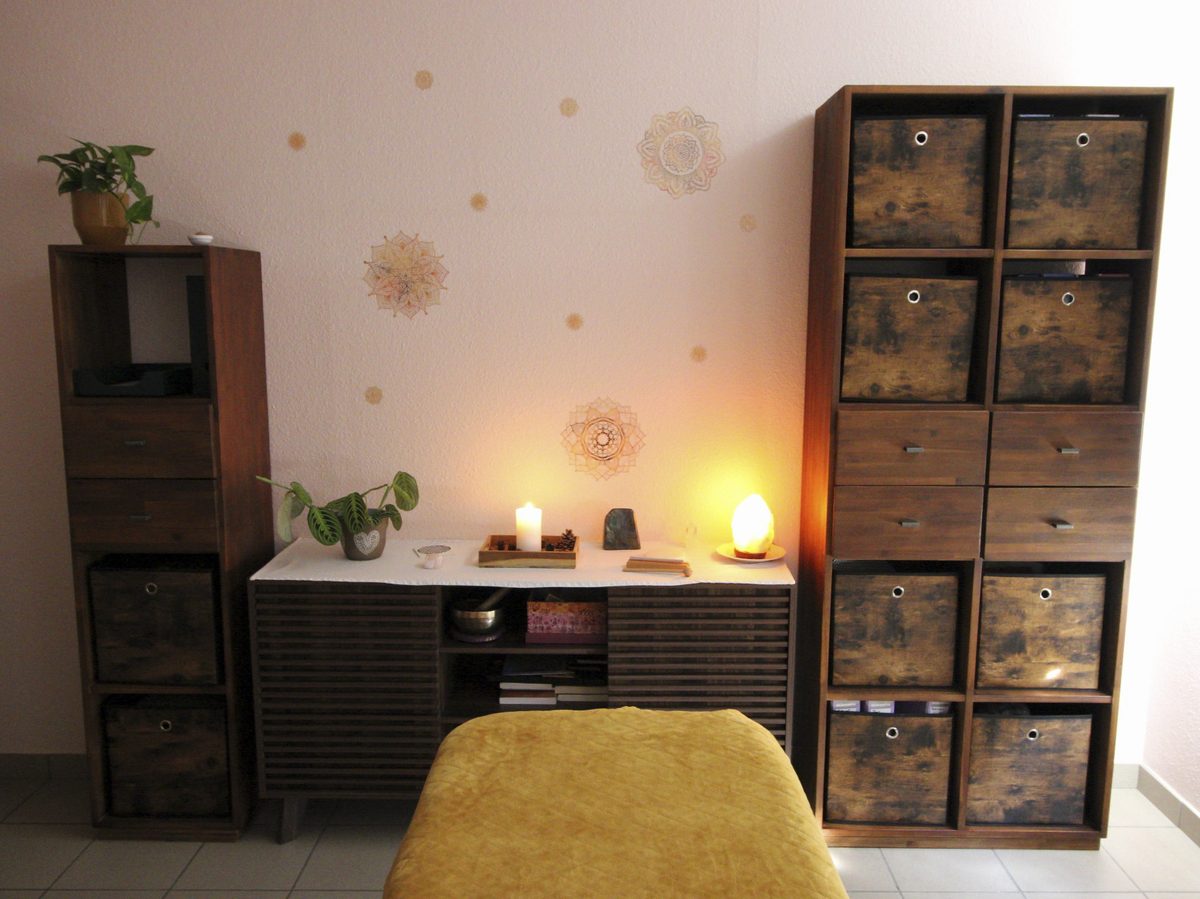 Meuble en bois avec bougie allumée, plantes vertes et lumière douce, sous des mandalas peints au mur
