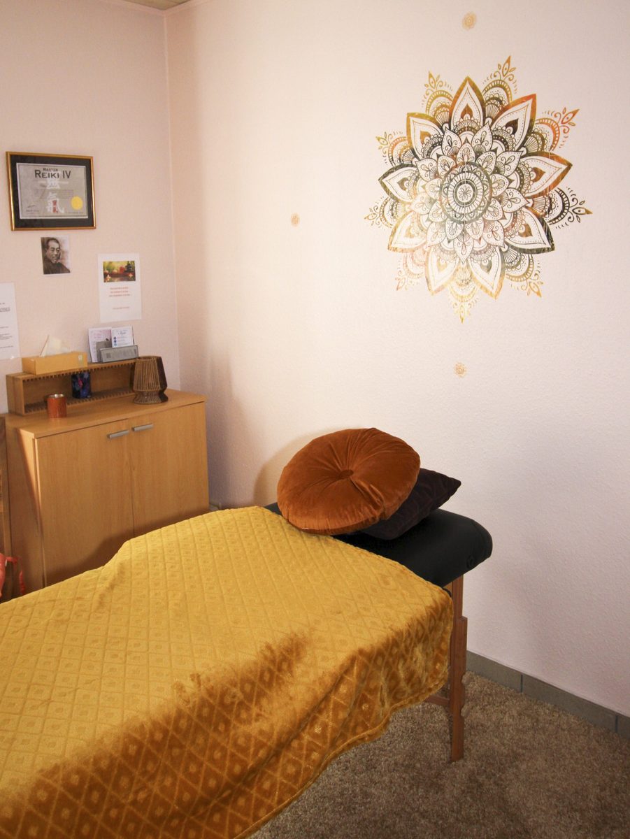 Table de soin Reiki recouverte d’une couverture dorée, coussins en velours, sous un mandala mural