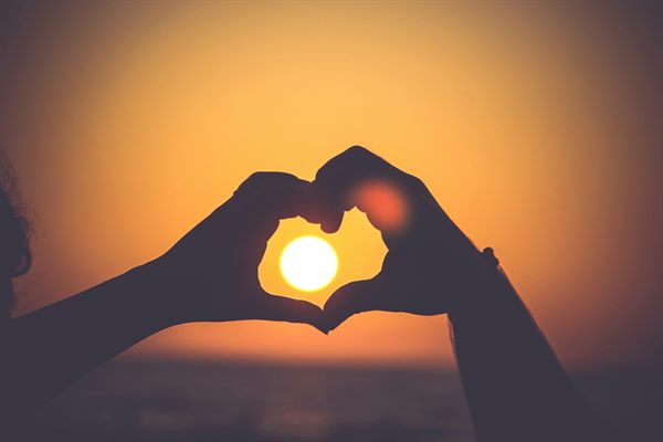 Deux mains formant un cœur autour du soleil couchant